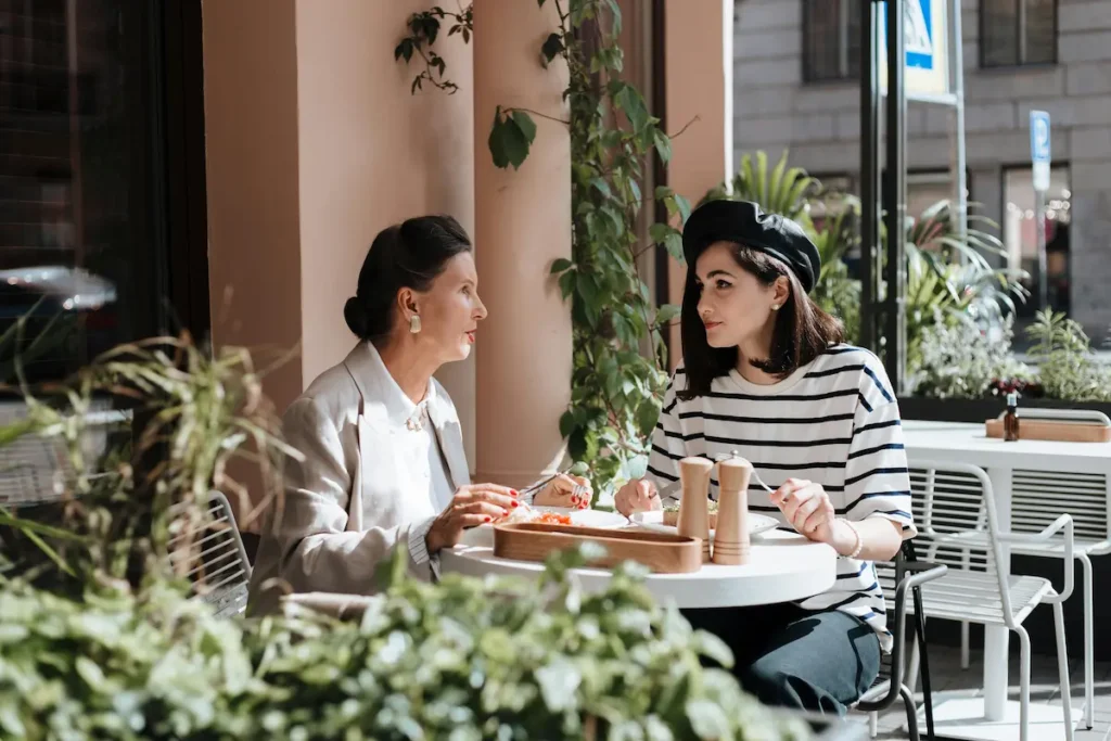 Madre e hija platicando de frente en una terraza de una cafetería , mostrando la comunicación y los retos de la relación con hijos adultos.